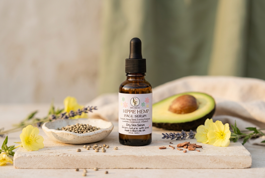 Hippie Hemp Facial Serum surrounded by avocado, hemp seeds, evening primrose flowers, and lavender in soft natural light.