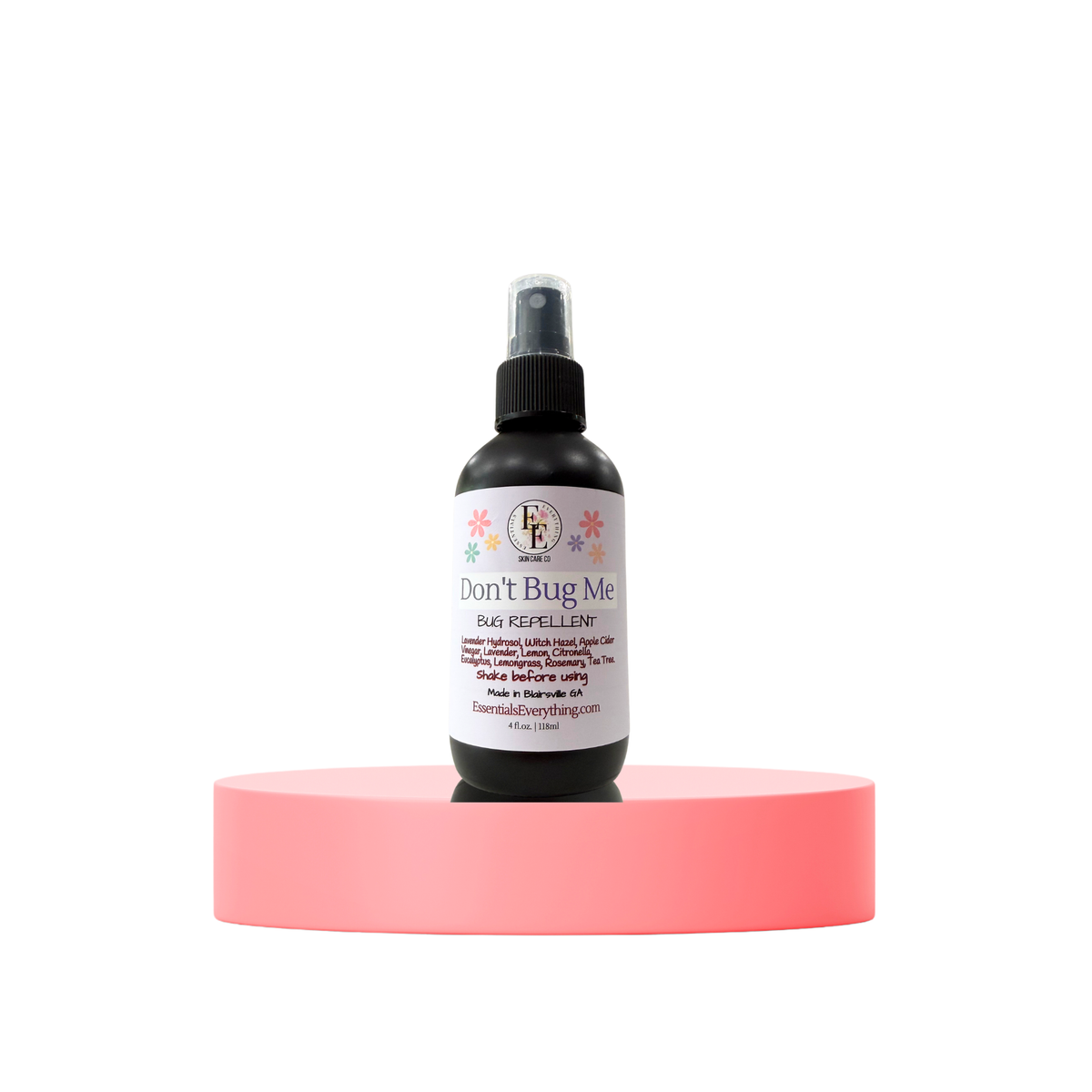 A small black spray bottle labeled 'Don't Bug Me Bug Repellent' stands centered on a round pink pedestal against a plain white background.